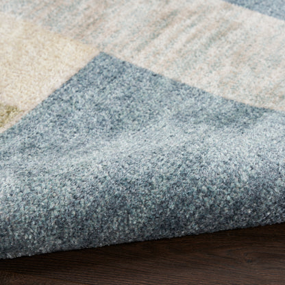 Blue-gray and beige geometric area rug with plush pile, folded edge on dark wood floor.