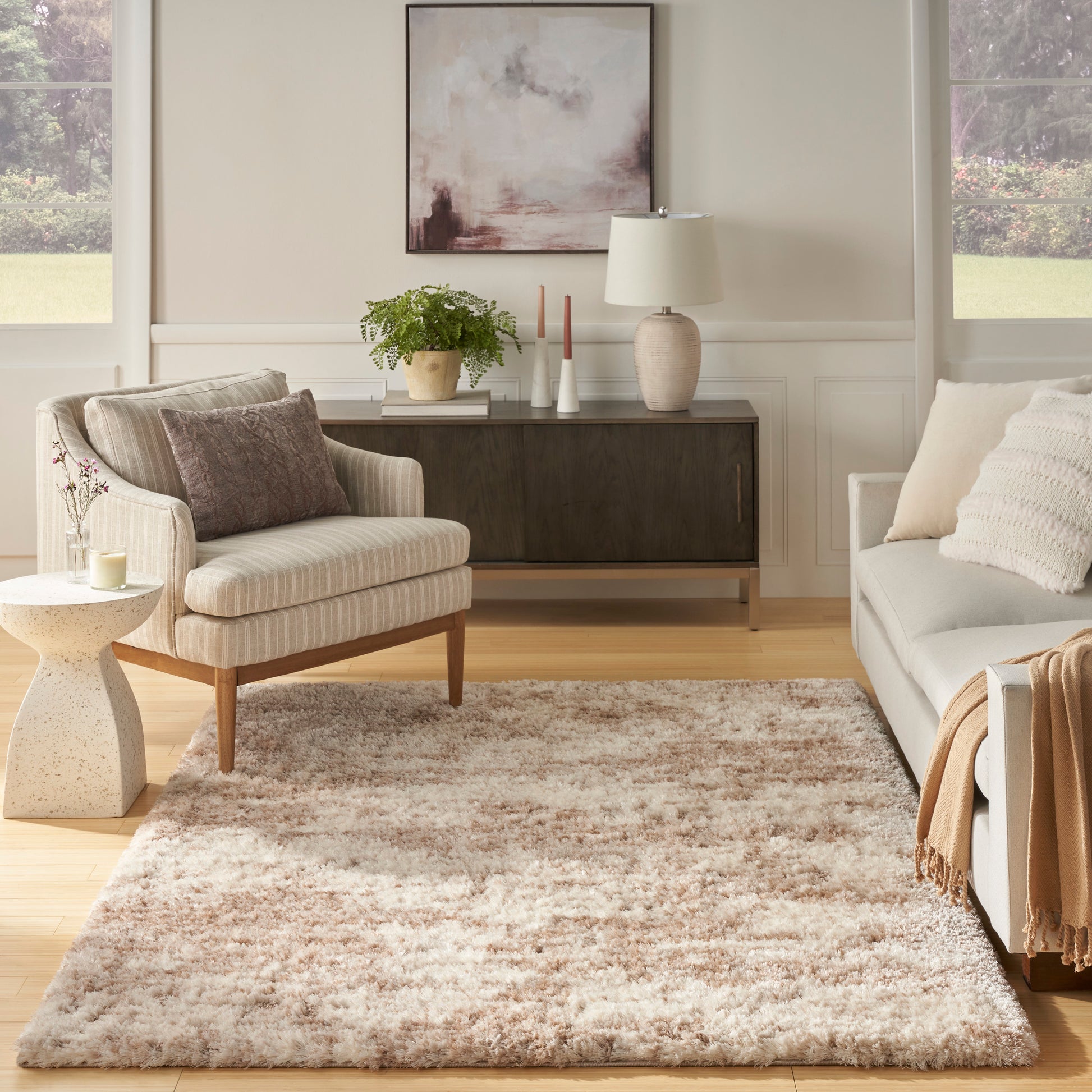 Neutral living room with beige striped armchair, shag rug, gray sofa, dark wood sideboard, plant, lamp, and abstract art.