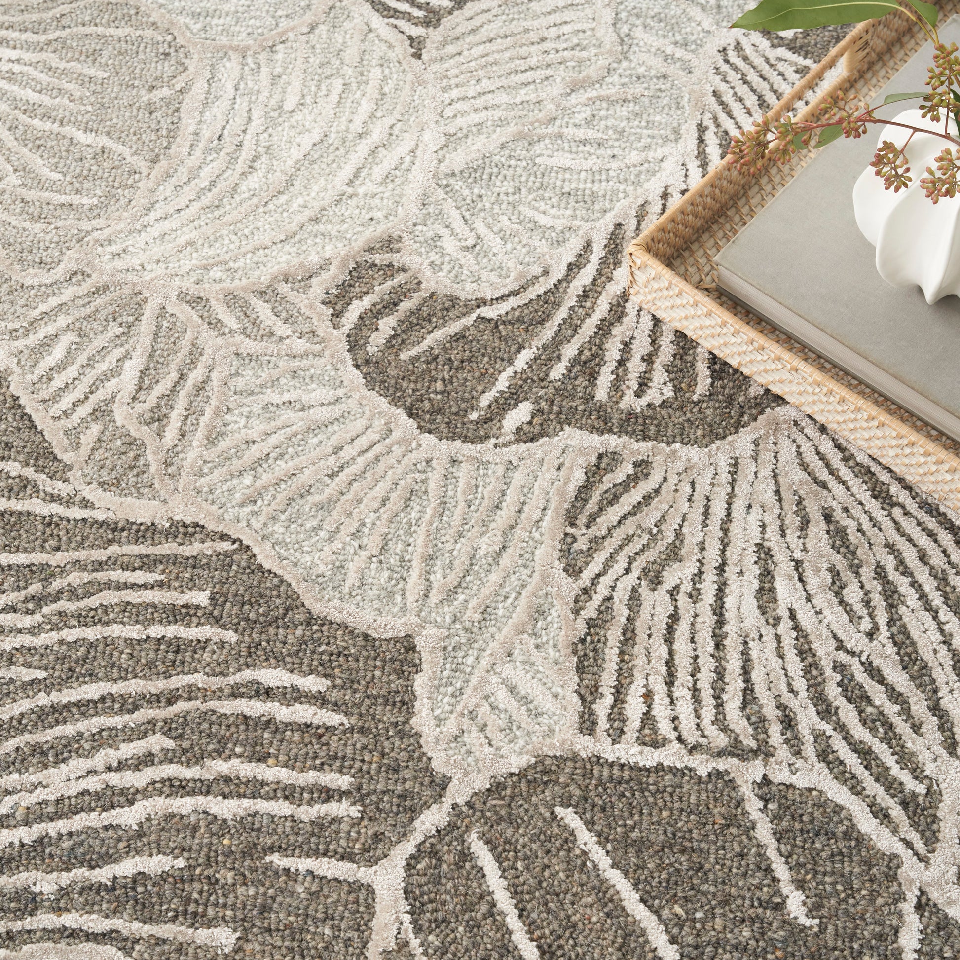 Beige and taupe leaf-patterned rug with plush pile; wicker tray and white decor visible in the corner.
