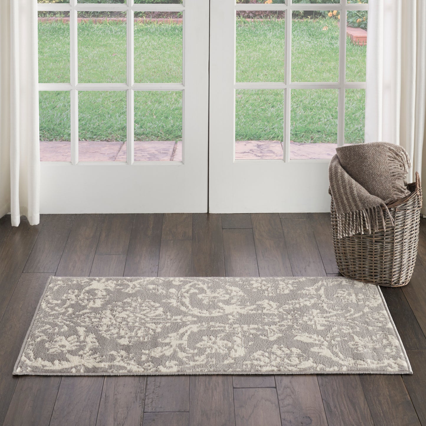Gray and ivory patterned rug runner on dark wood floor beside glass French doors, with a wicker basket and blanket.