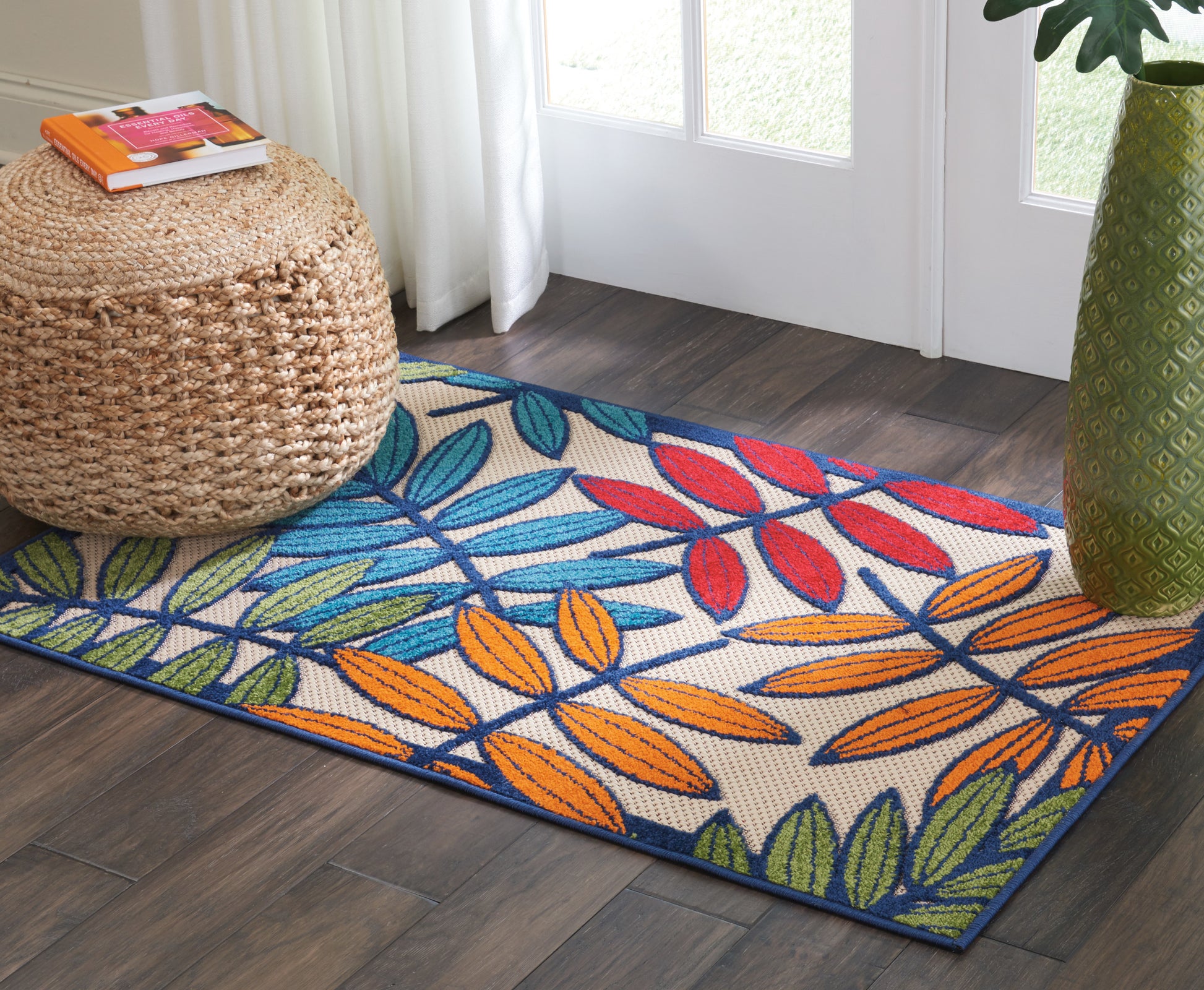 Colorful rectangular area rug with blue, orange, red and green tropical leaf pattern on cream; woven texture in a modern living room.