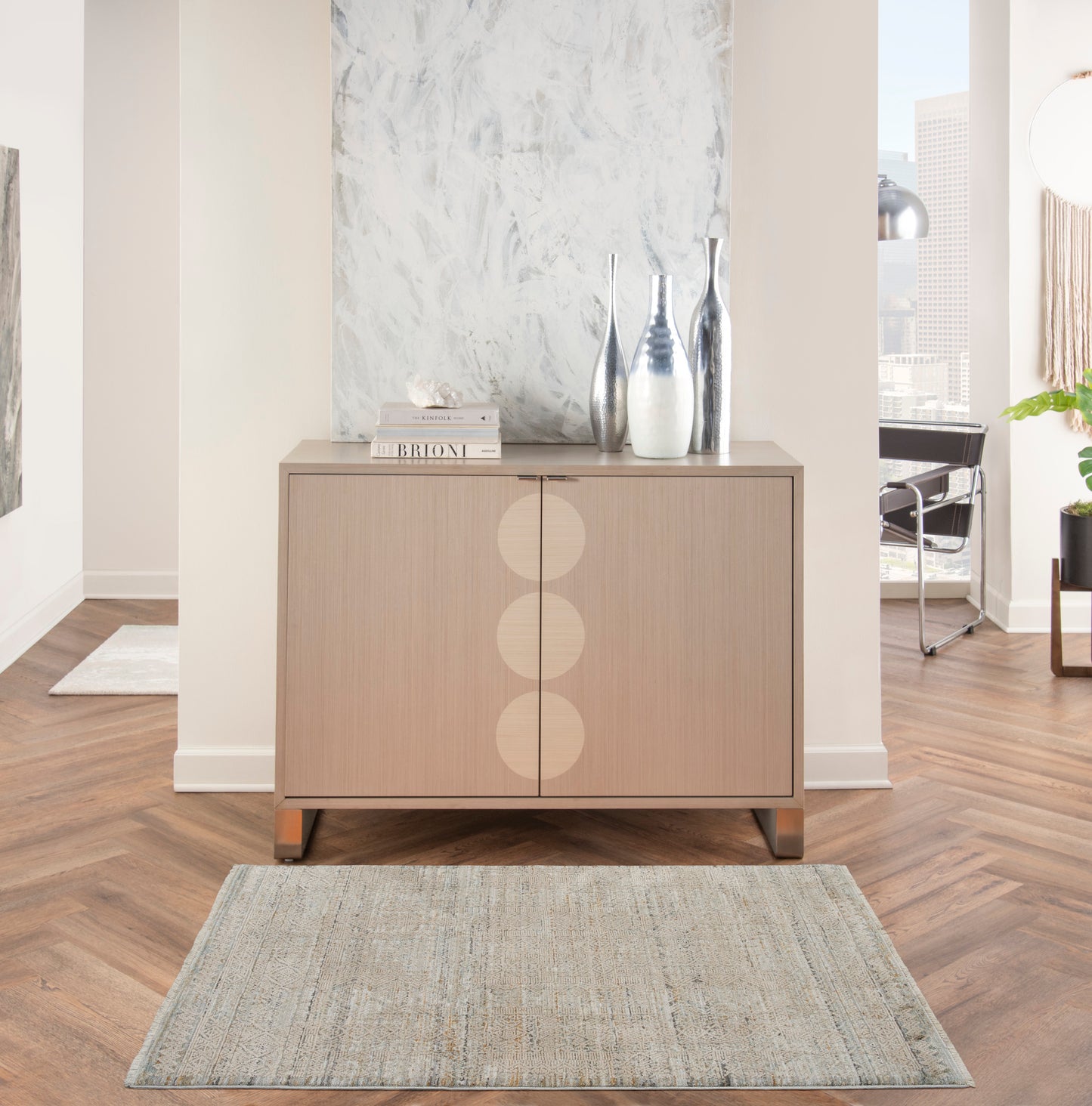 Light wood sideboard with three circular inlays, metal legs, topped with vases and books in a modern living room.