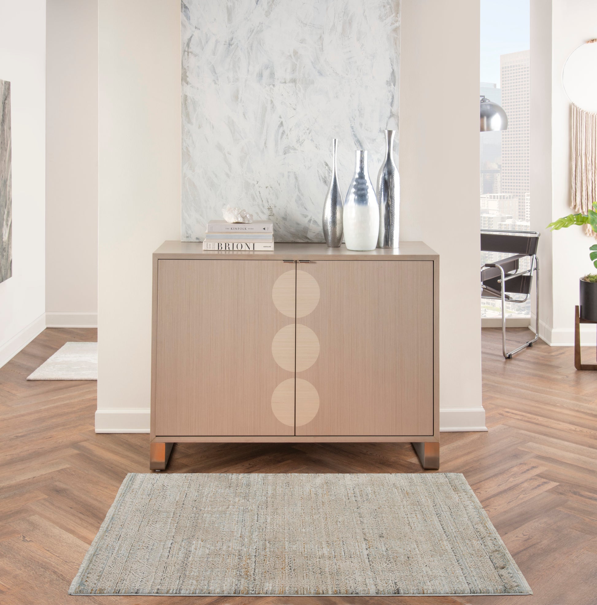 Light wood sideboard with three circular inlays, metal legs, topped with vases and books in a modern living room.