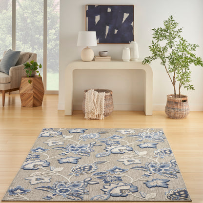Beige woven area rug with blue floral pattern on light hardwood floor, living room with console table and potted plant.