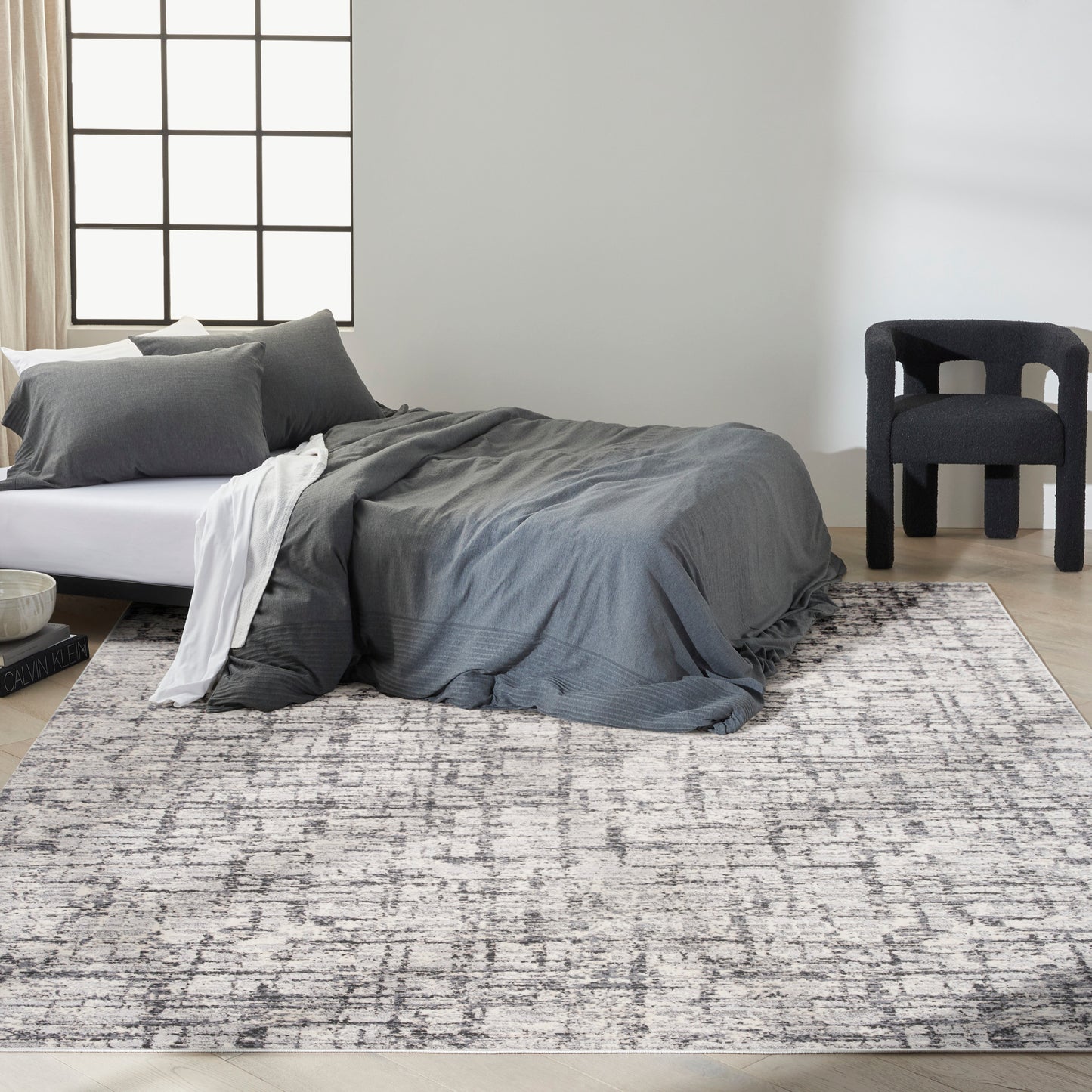 Modern gray bedroom with low white bed, charcoal duvet, white sheet, and a large patterned gray rug.
