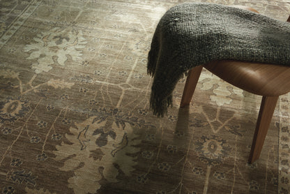 Close-up of a brown patterned area rug with floral medallions and a fringed dark throw draped over a wooden chair leg.