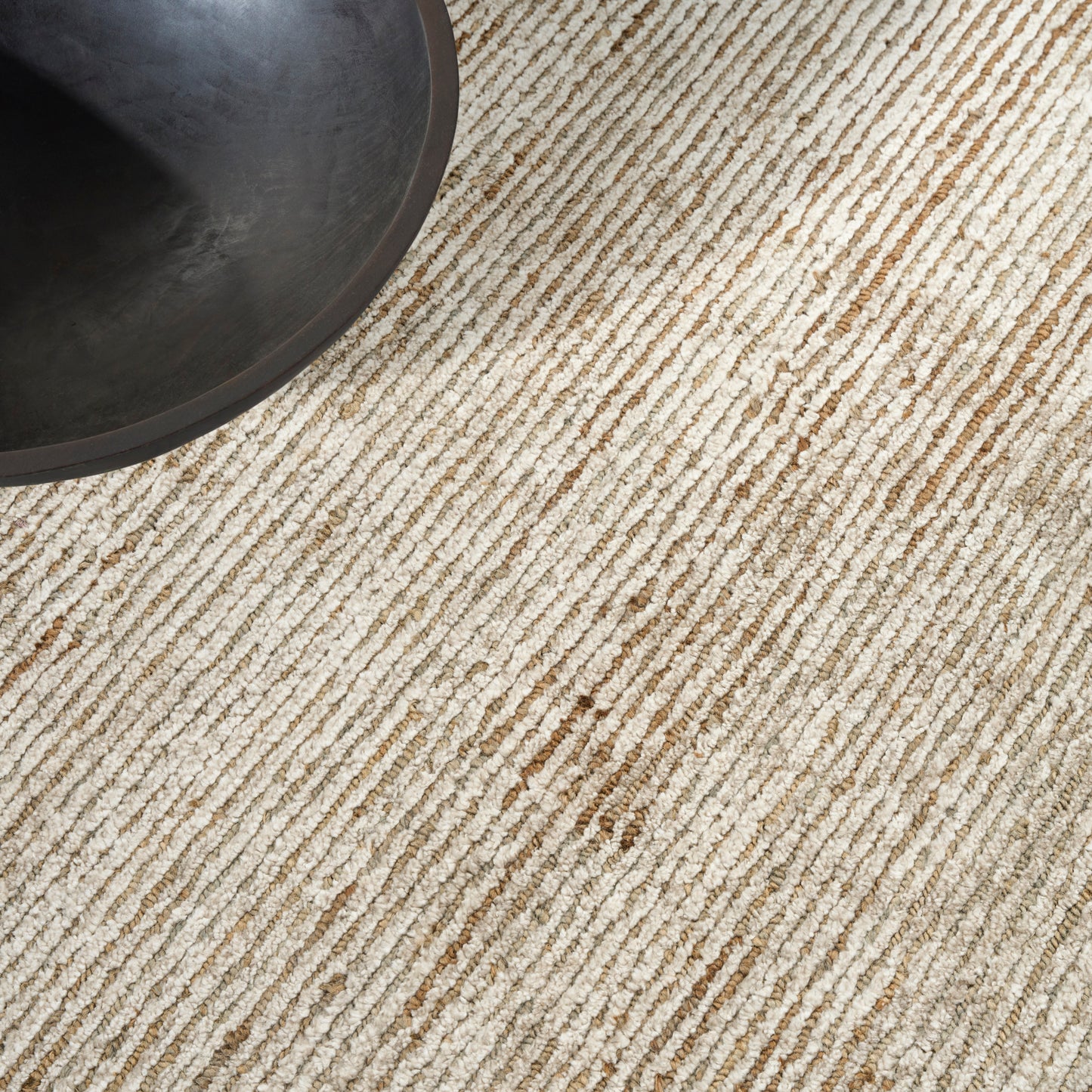 Beige striped textured rug with a dark round bowl in the top-left corner; small brown stain.