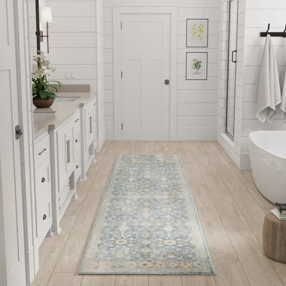 Long blue-and-ivory patterned runner rug in a white bathroom with wood floor, dual vanity, freestanding tub & framed botanicals.
