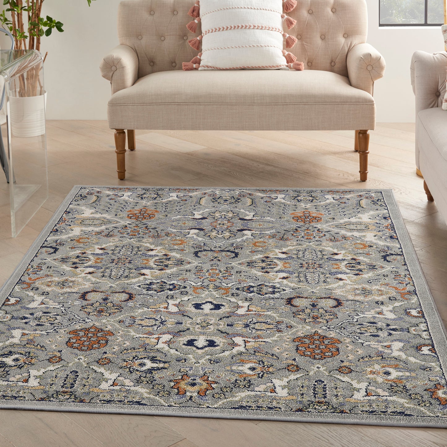 Blue-gray area rug with ivory & orange floral motifs on a light wood floor beside a beige tufted sofa.