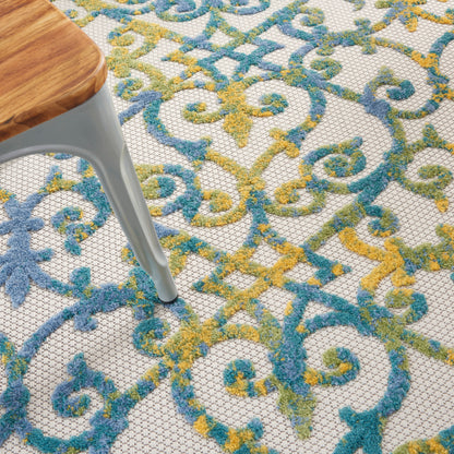 Close-up of an ornate rug with blue, teal & yellow scrollwork; light gray metal-legged wooden stool resting on it.