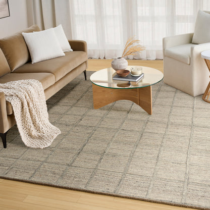 Round glass coffee table with curved base, beige sofa with white pillows and knit throw, white armchair, gray rug.