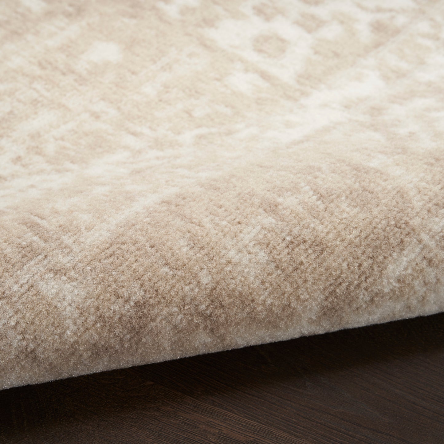 Beige plush area rug with soft, fluffy texture in cream tones on dark wood floor.