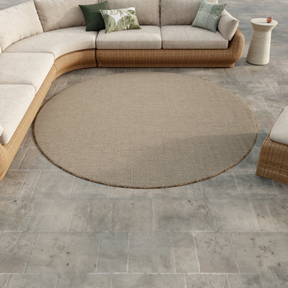 Round beige woven outdoor rug on gray tile, curved wicker sectional with green and palm-leaf cushions