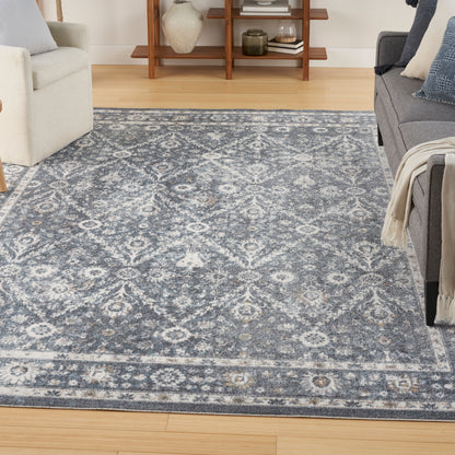 Rectangular blue-gray area rug with ivory damask medallion pattern in a cozy living room.