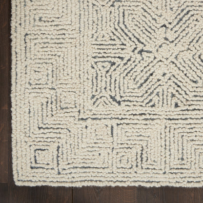 Cream shag rug with blue-gray geometric maze patterns and border, plush looped pile on dark wood floor.