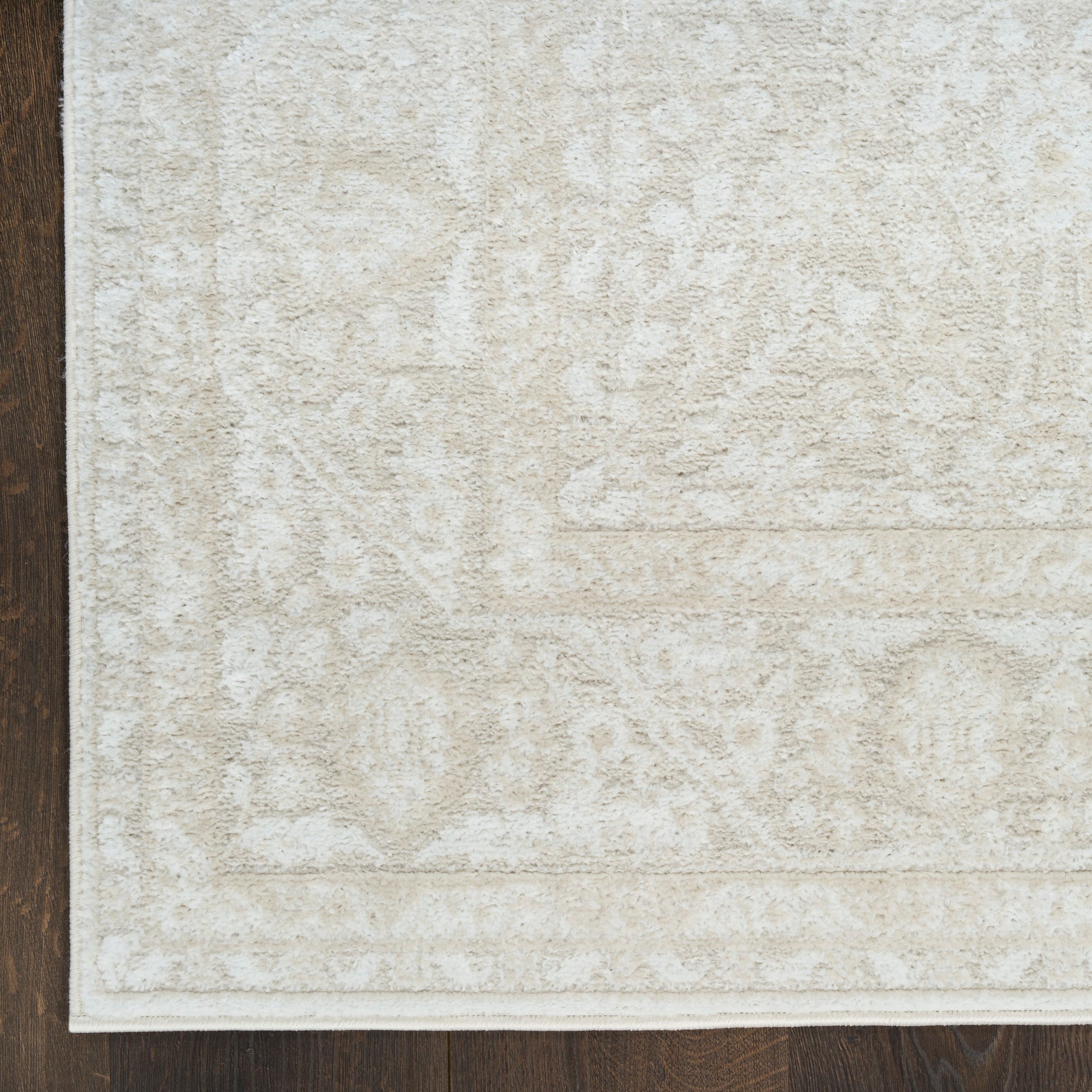Cream-beige area rug with subtle traditional motifs and a light border on dark wood floor.