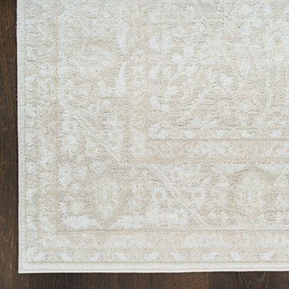 Cream-beige area rug with subtle traditional motifs and a light border on dark wood floor.