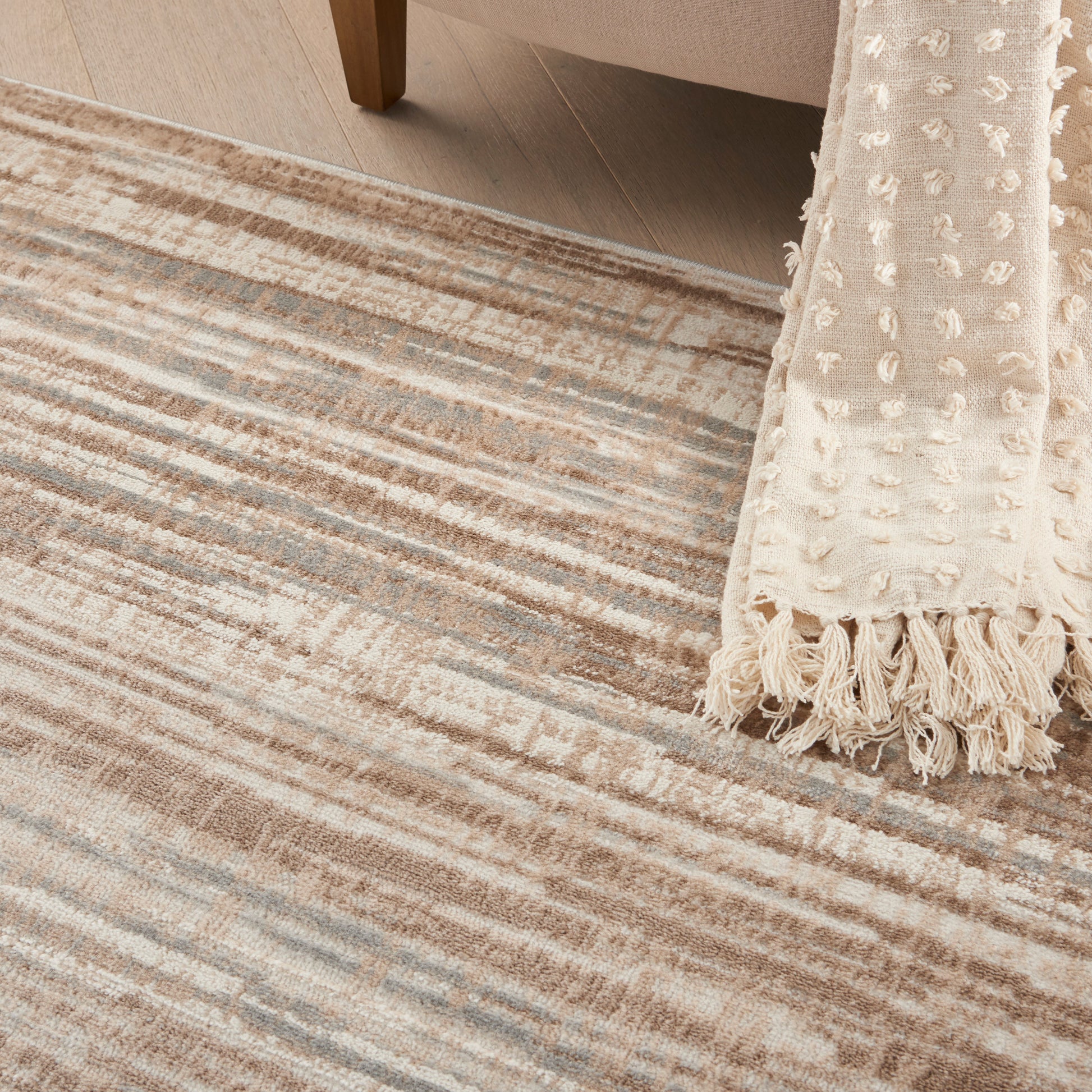 Beige striped rug with cream tones and a textured cream throw with tassels draped at the edge