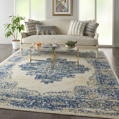 Blue-and-cream patterned rug in a living room, with a beige tufted sofa, round glass coffee table, potted plant, and framed art.