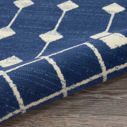 Navy blue woven rug with white geometric diamonds and lines, folded edge on a wooden floor.