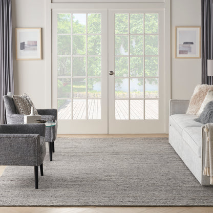 Modern gray living room: light gray sofa, two charcoal armchairs, glass side table, textured rug, white French doors.
