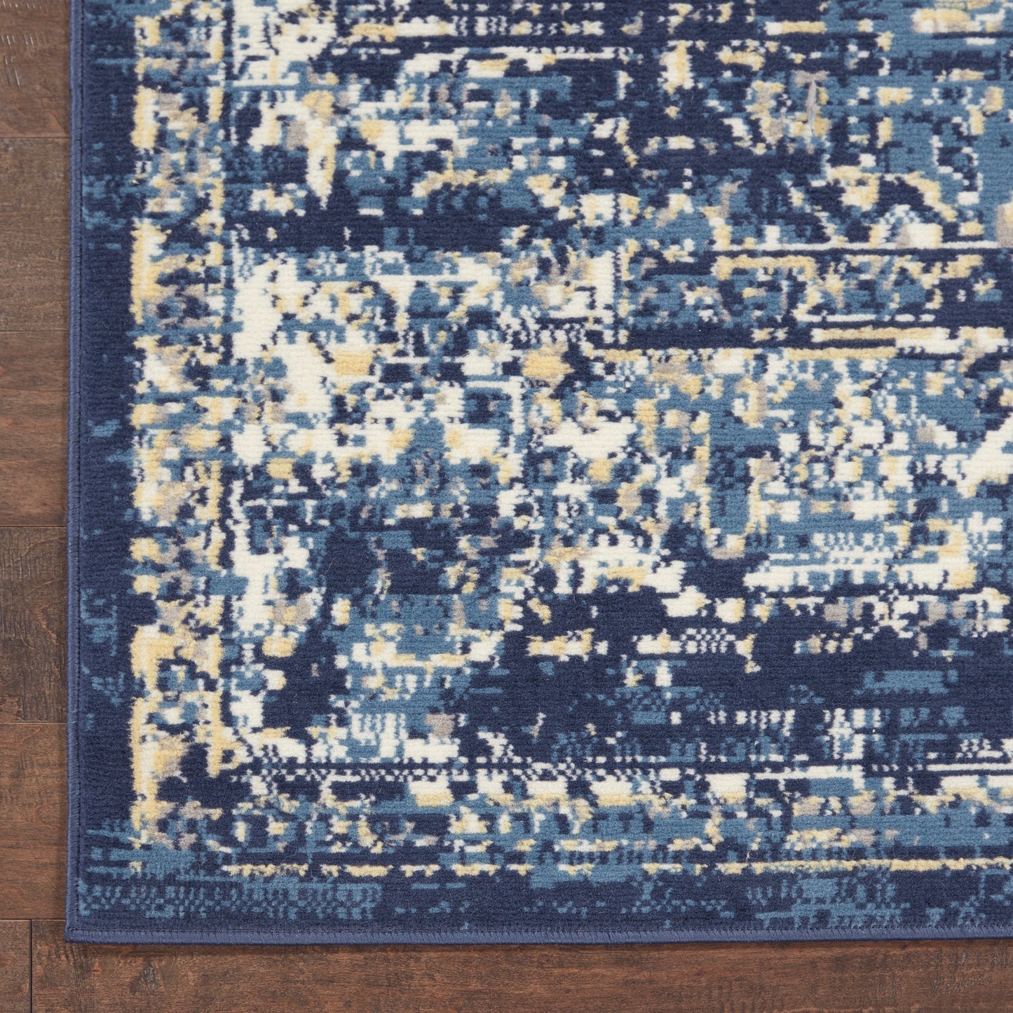 Rectangular abstract-pattern rug in navy, blue and cream with a dark blue border on a wooden floor.