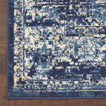 Rectangular abstract-pattern rug in navy, blue and cream with a dark blue border on a wooden floor.