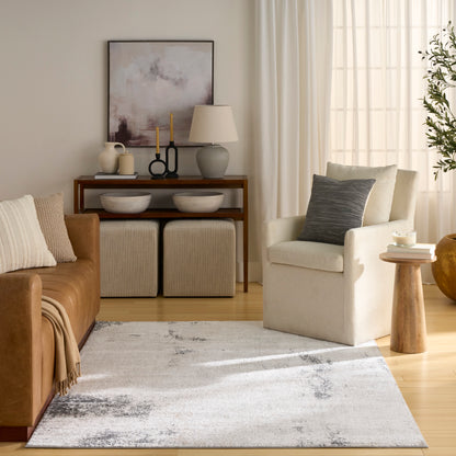 Neutral living room with tan leather sofa, cream armchair, abstract rug, wooden console, two ottomans, lamp, plants.