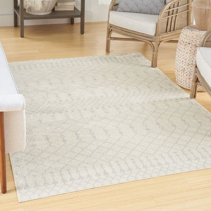 Light gray geometric patterned area rug on pale wood floor with rattan seating in a cozy living room.
