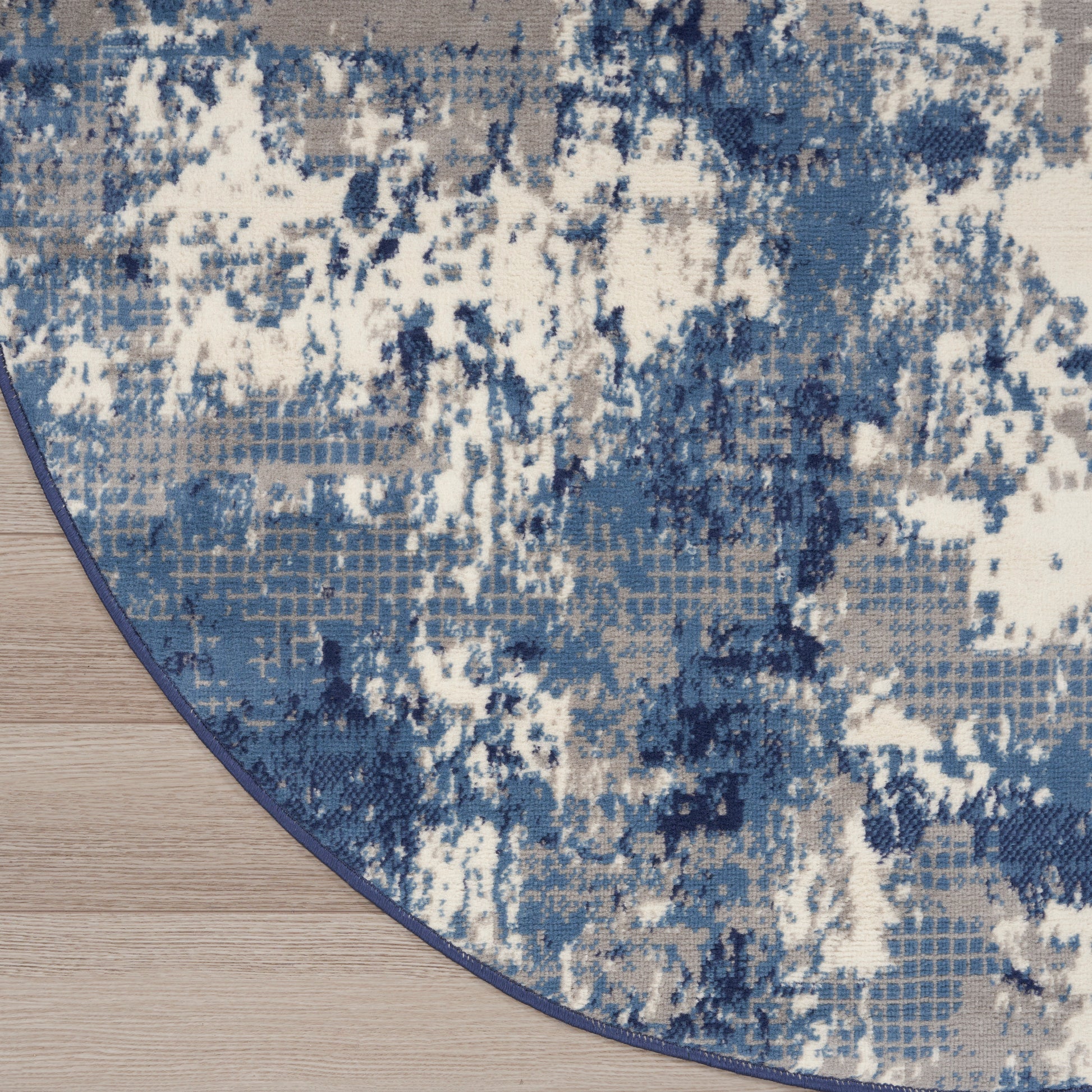 Round rug featuring an abstract blue and white pattern with a dark blue edge on a light wood floor.