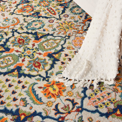Colorful floral woven rug with ivory base in blues, oranges, greens; white textured throw with fringe draped over edge.