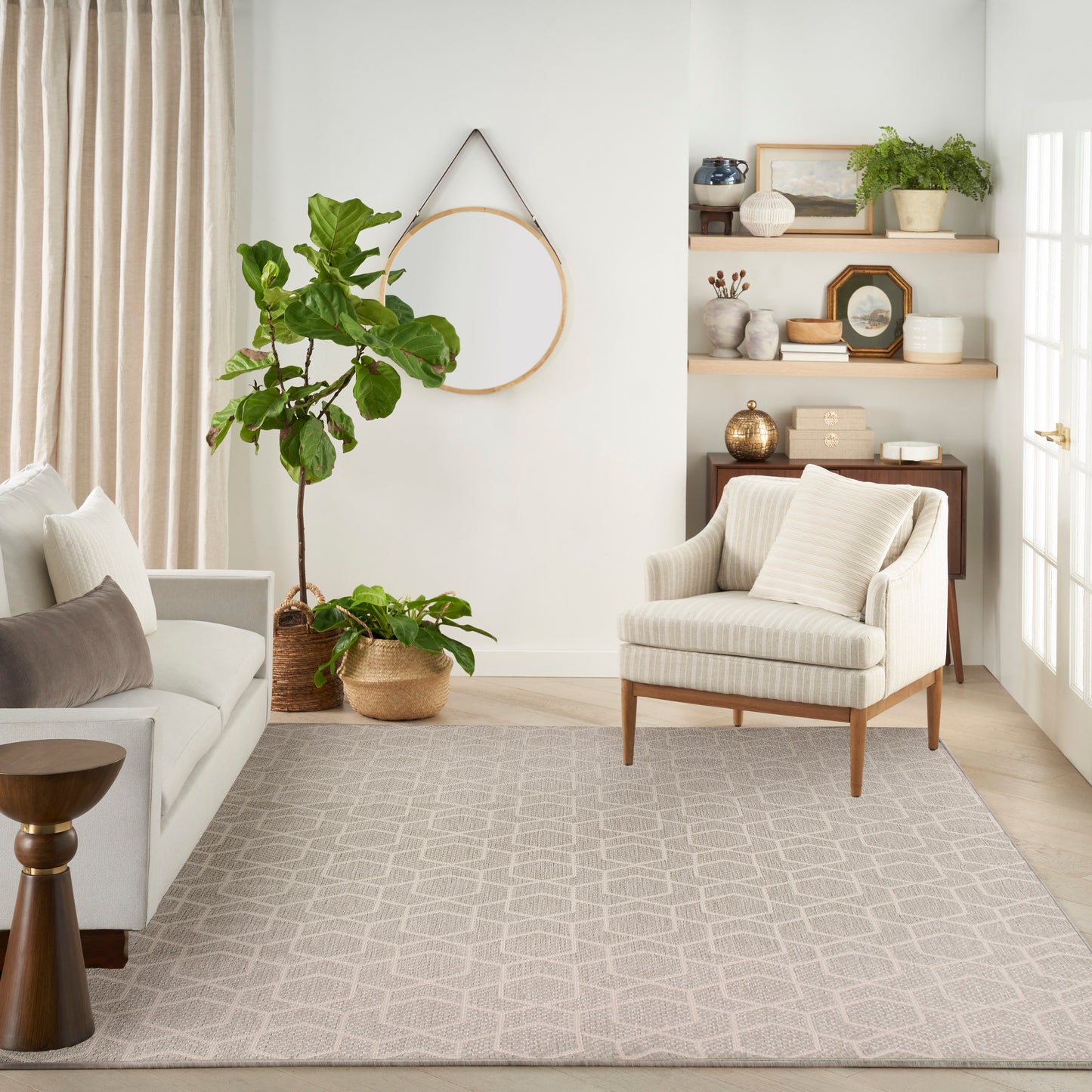 Neutral living room with gray sofa, striped beige armchair, tall fiddle-leaf fig plants, woven rug, and open shelving.