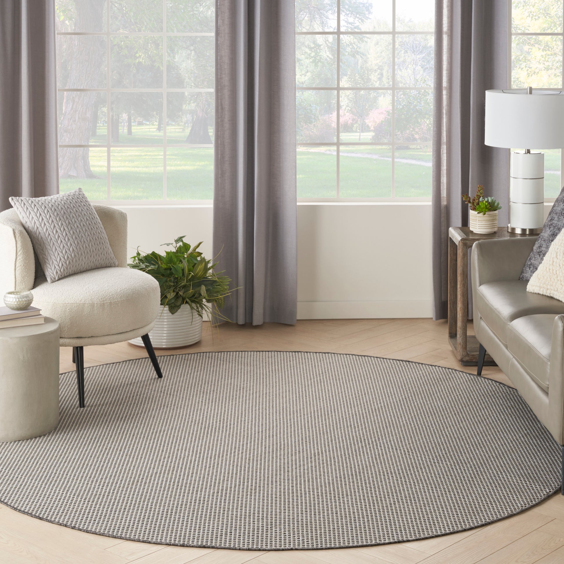 Round gray striped area rug on light wood floor in a bright living room with a beige sofa, plants, and gray curtains.