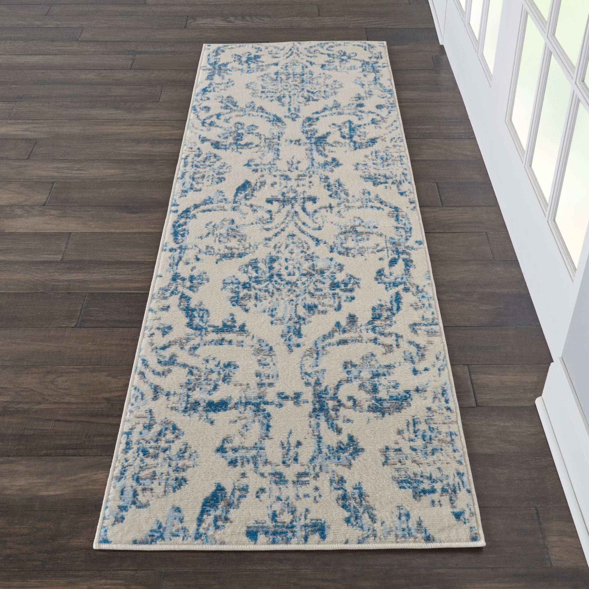 Beige and blue damask runner rug, long rectangular, on dark wood floor near white-framed windows.