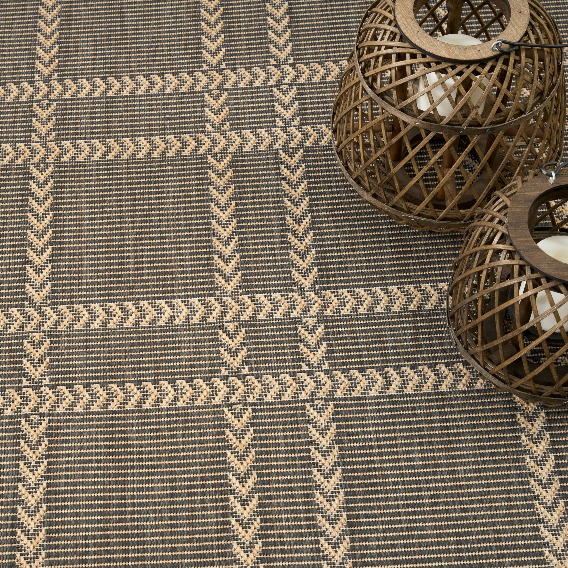 Woven rug with beige chevron pattern on gray background; two round brown wicker lanterns with candles.