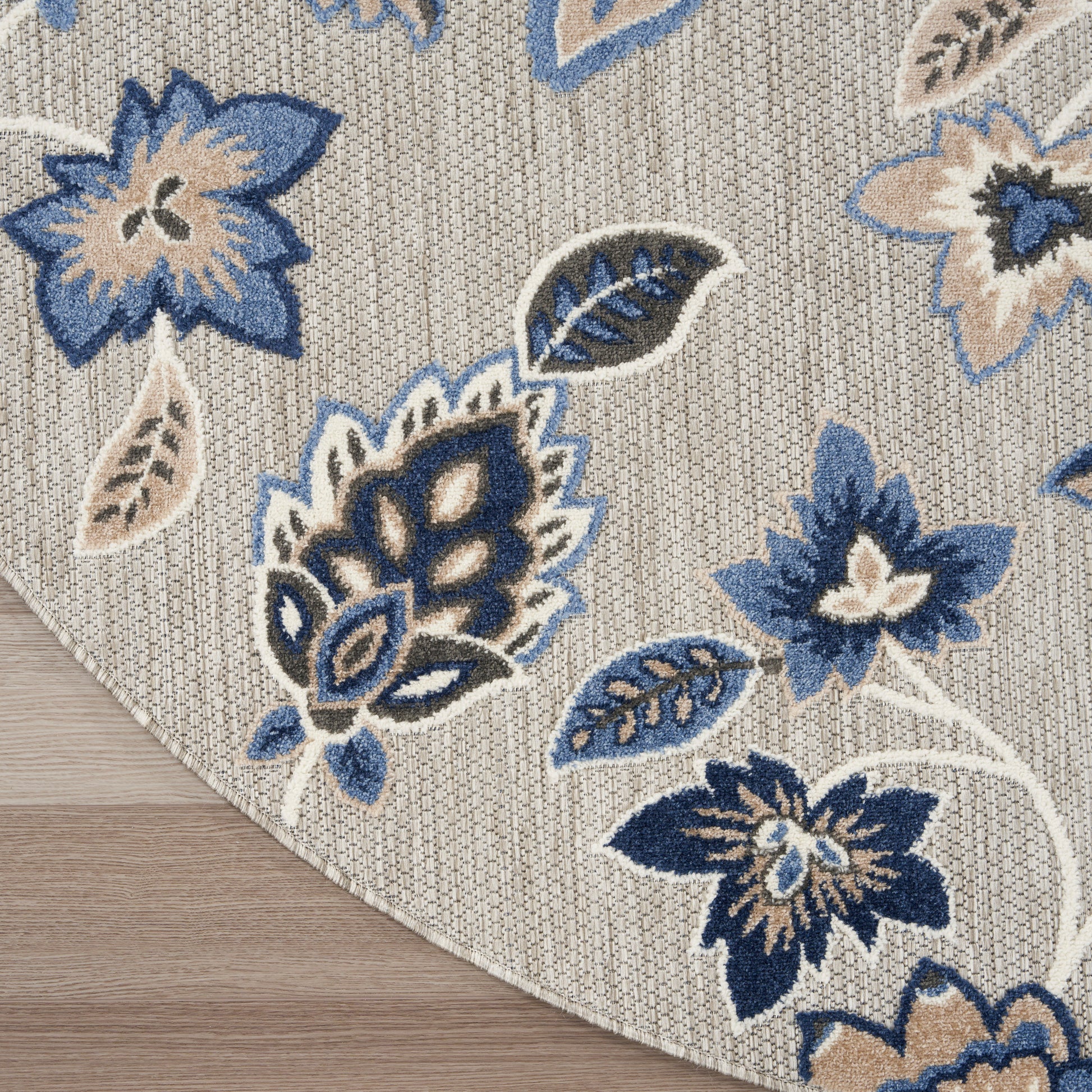 Beige woven round rug with blue floral pattern in navy & light blue, leaf accents, and curved edge on wood floor.
