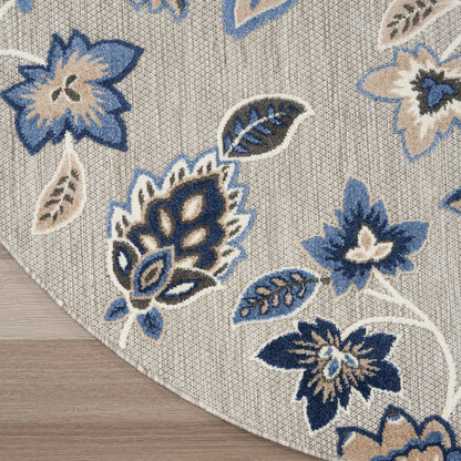 Beige woven round rug with blue floral pattern in navy & light blue, leaf accents, and curved edge on wood floor.