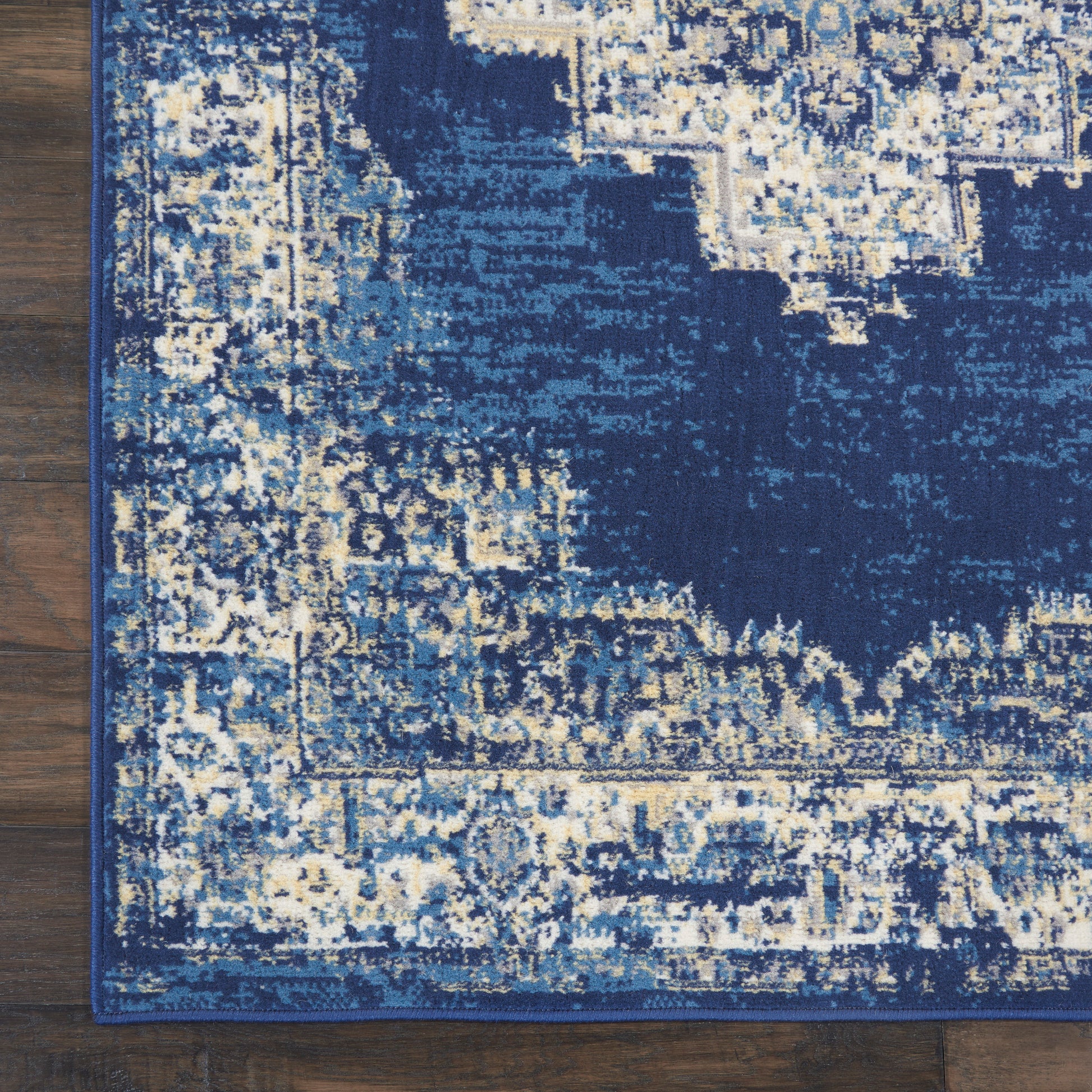 Deep blue distressed area rug with cream and light-blue pattern and border on a wooden floor.