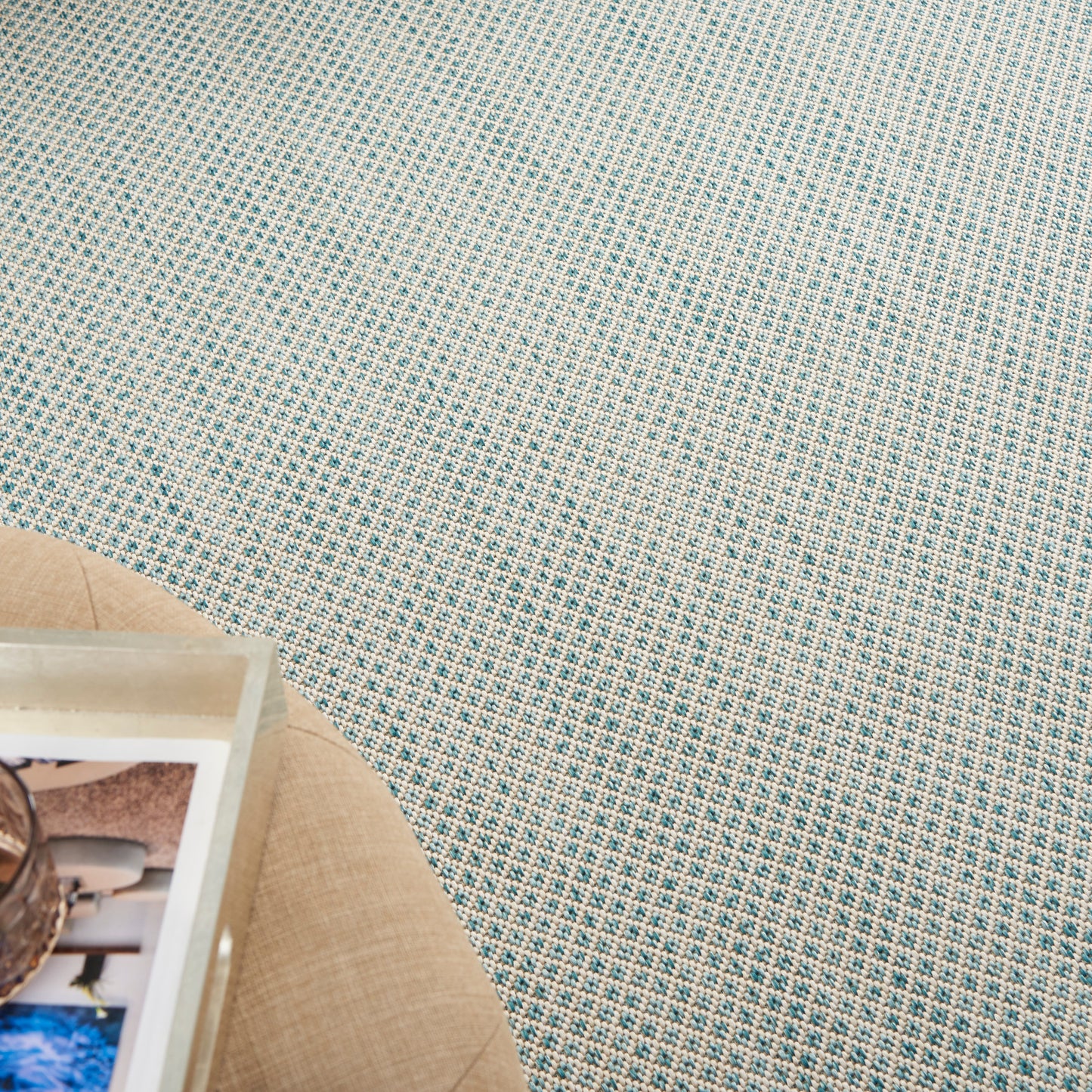 Blue-green woven fabric with a tiny white grid pattern; beige round placemat and white tray of photos in lower-left corner.