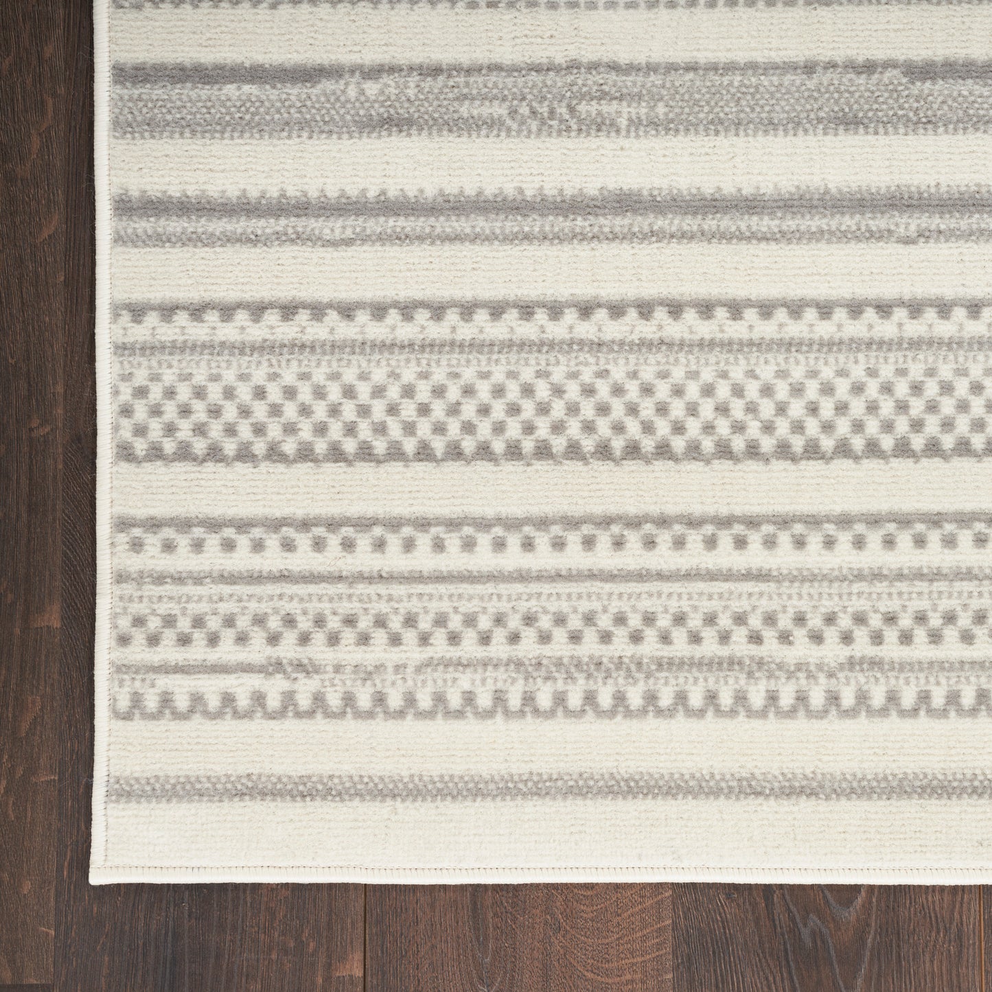Cream and gray striped woven rug with geometric patterns on dark wooden floor.