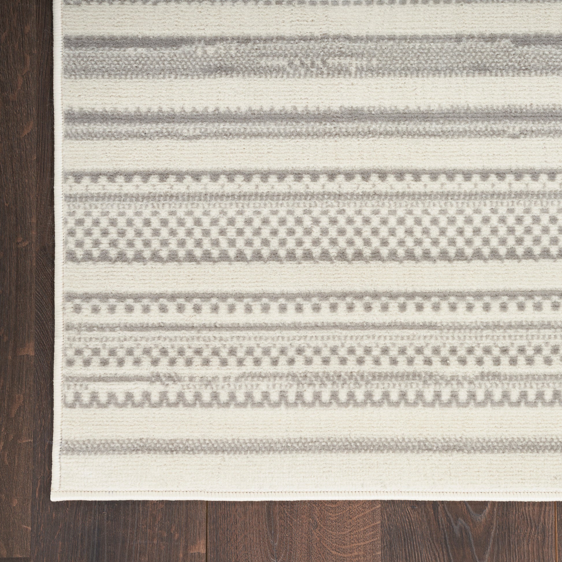 Cream and gray striped woven rug with geometric patterns on dark wooden floor.