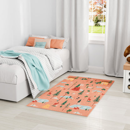Peach-colored kids' rug with trees and camp motifs in teal and white, on a pale wood floor beside a white bed.