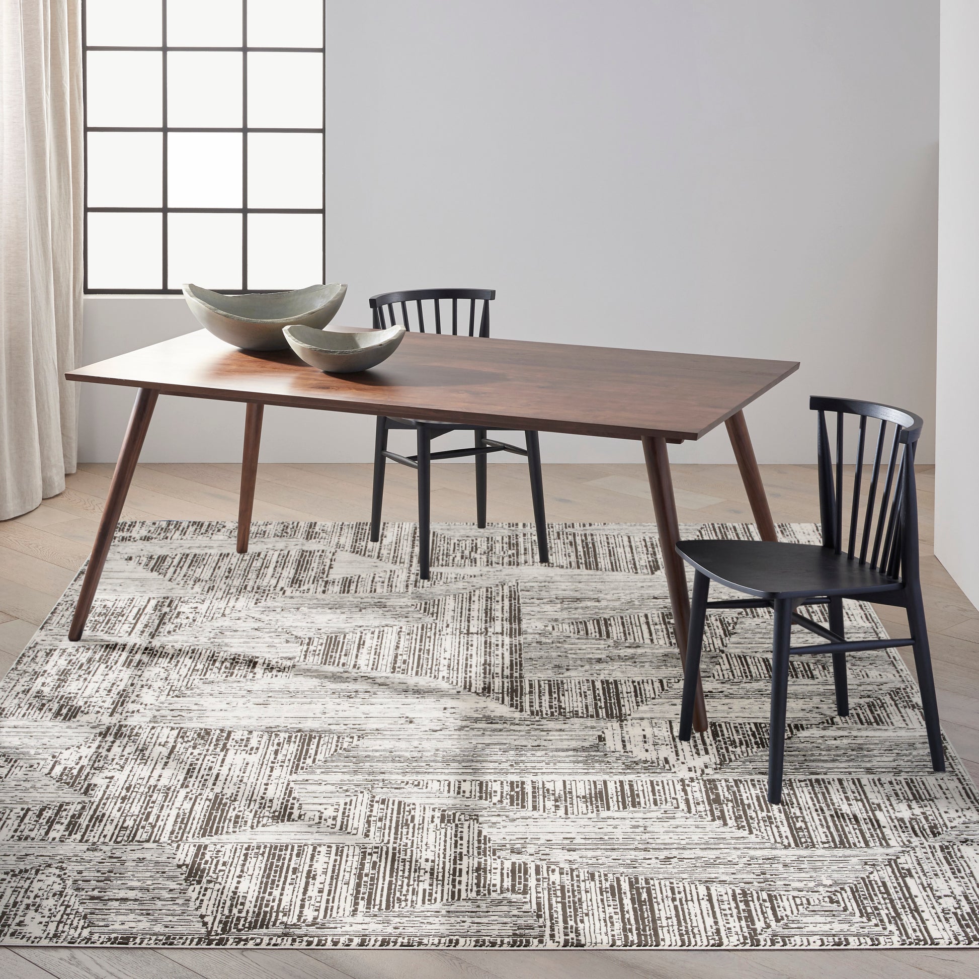 Walnut mid-century dining table with tapered legs, black chairs, ceramic bowls, on a geometric monochrome rug.