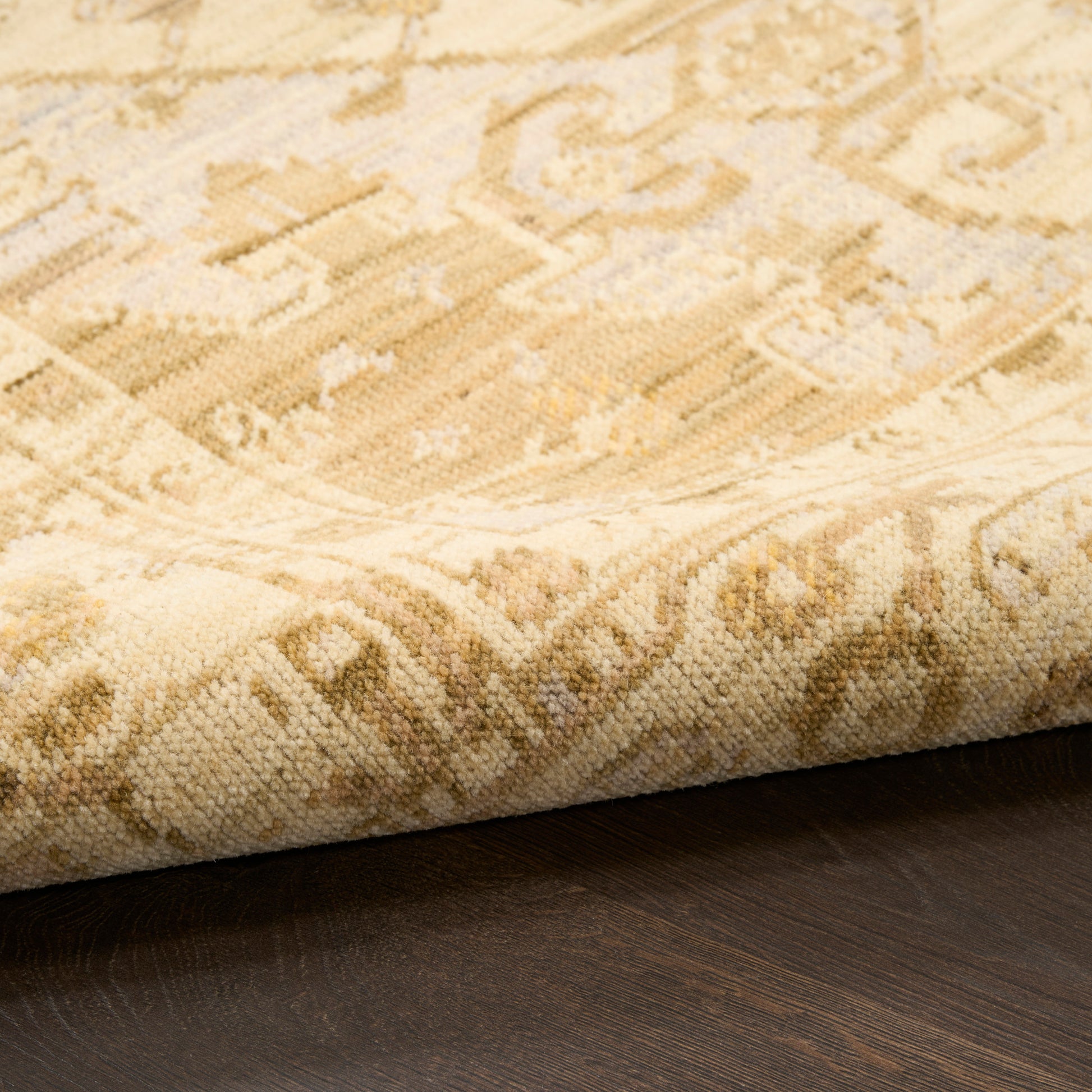 Beige oriental rug with gold geometric motifs, partially rolled at edge over dark wood floor