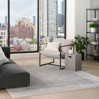 Light gray modern rug in a contemporary living room with a gray sofa, beige armchair, concrete side table, and plants.