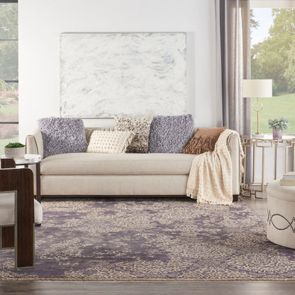 Beige sofa with lavender pillows, cream knit throw, marble wall art, purple rug, and gold side table in a bright living room.