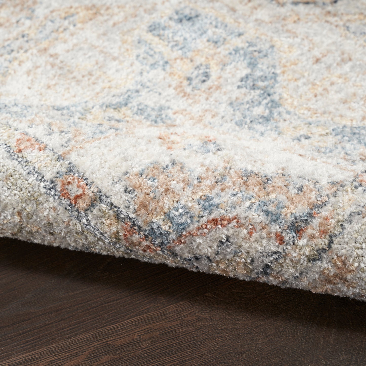 Close-up of a plush area rug with cream, blue, beige and tan geometric pattern on dark wood floor.