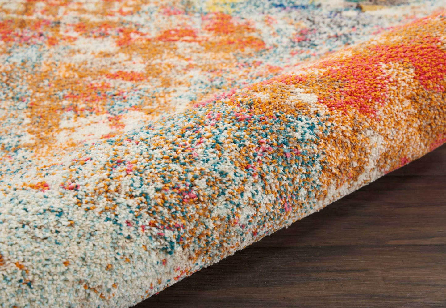 Colorful high-pile shag rug with orange, blue, pink, white and yellow tones; plush abstract pattern on dark wood floor.