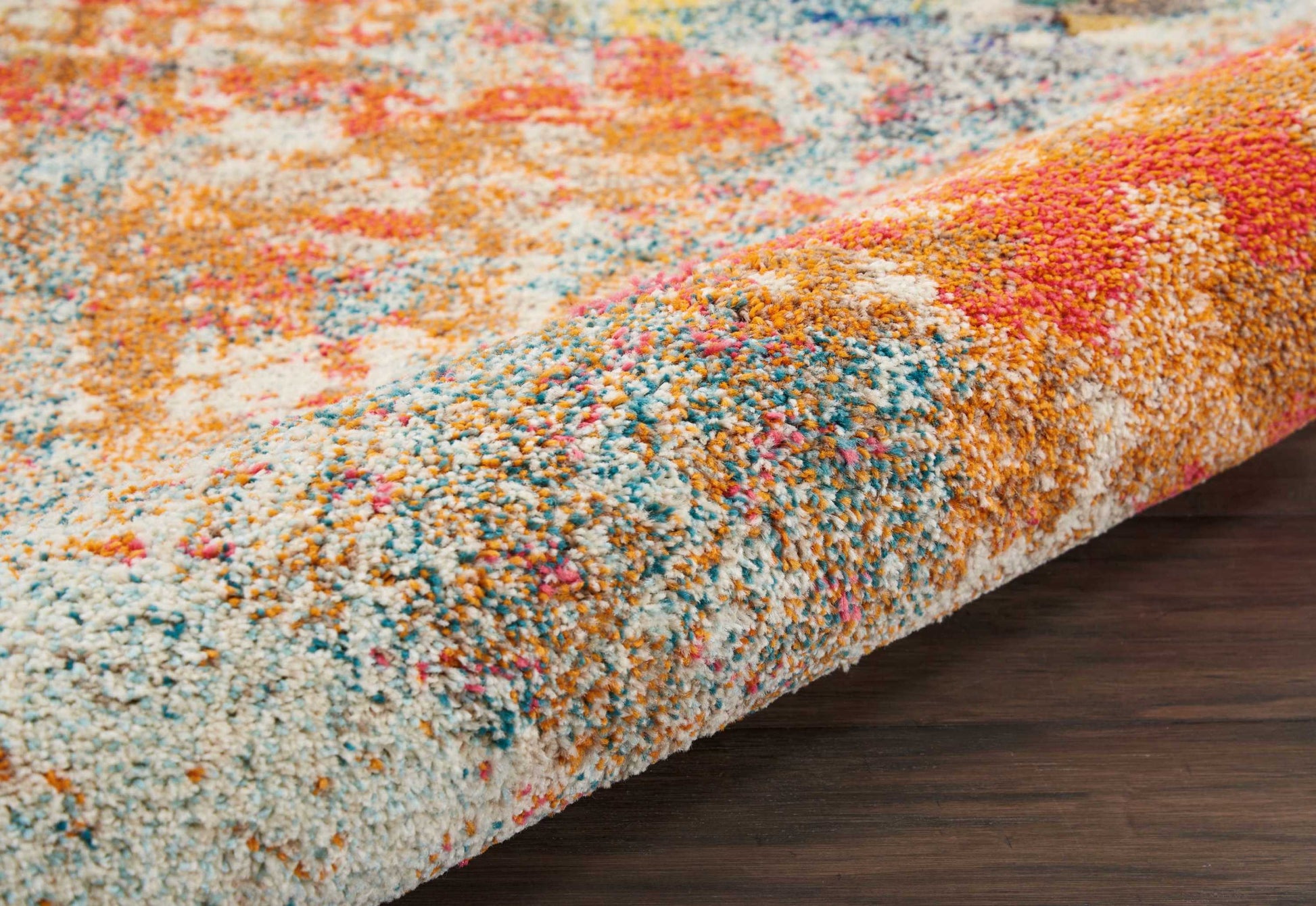 Colorful high-pile shag rug with orange, blue, pink, white and yellow tones; plush abstract pattern on dark wood floor.