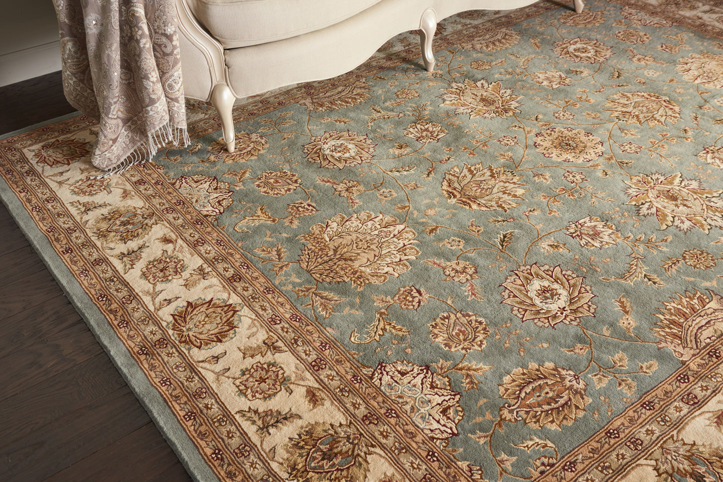 Traditional Persian-style area rug in blue with cream floral motifs and an ornate border under a beige sofa.